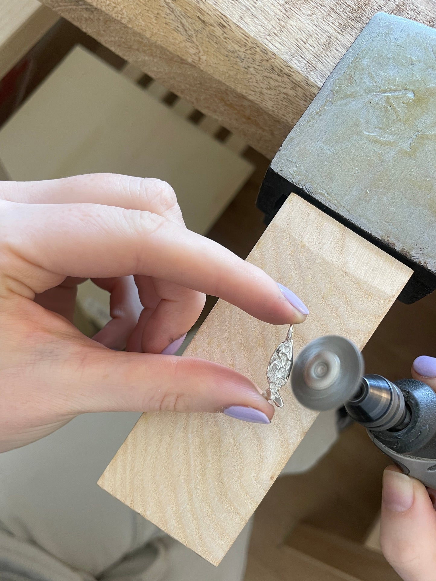 Person using a drill to work on a piece of jewelry with a wooden block.
