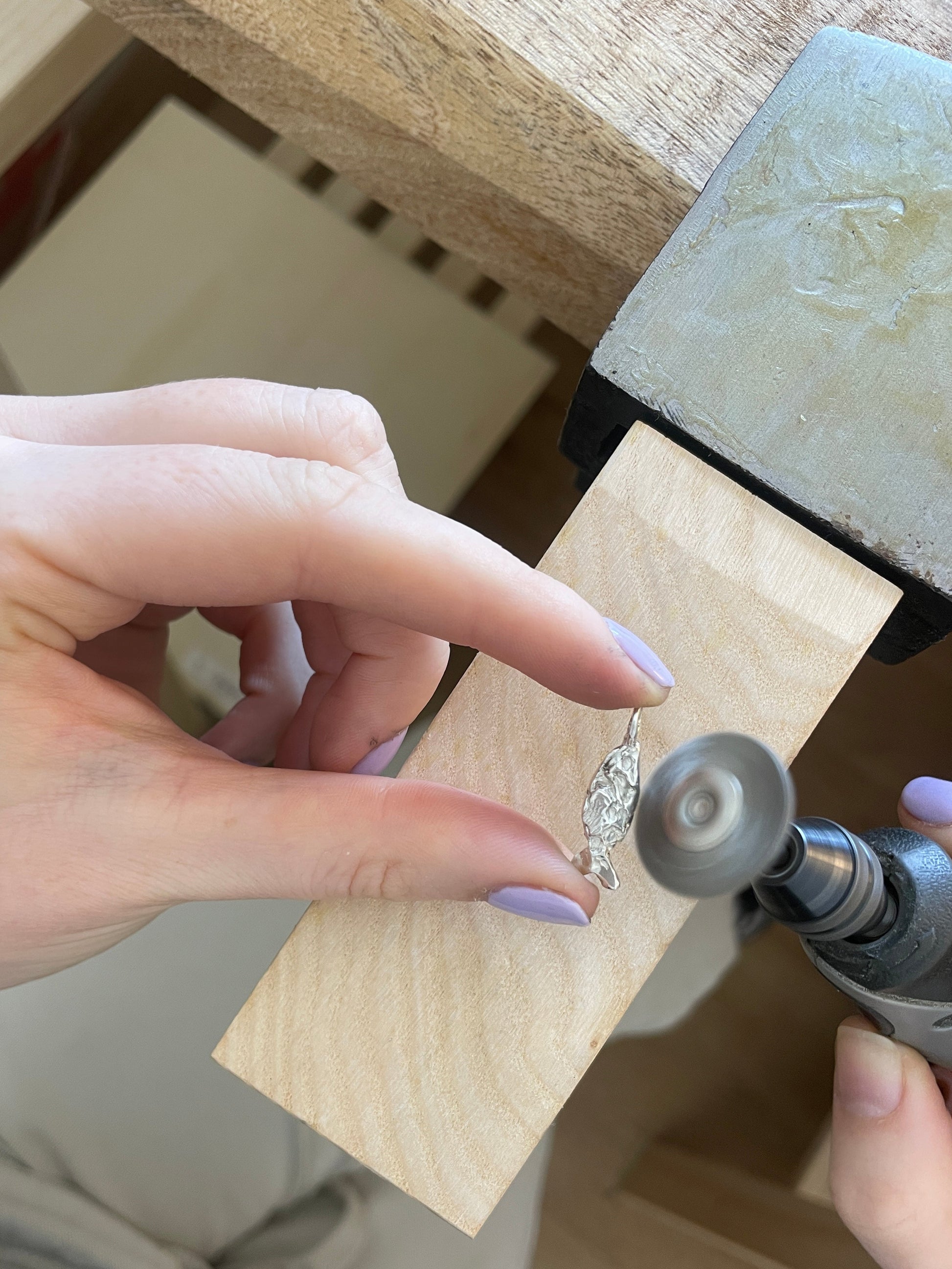 Person using a drill to work on a piece of jewelry with a wooden block.